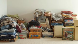 家の中で不要品を整理している様子、衣類や本、ゲーム、古い家電をまとめているシーン、シンプルで清潔感のある写真風、温かい色合